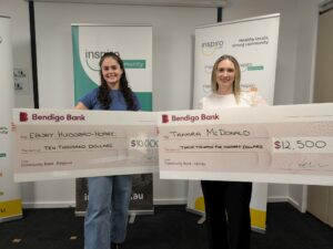 Inspiro 2025 Tertiary Health Scholarship Winners Ebony and Tamara, standing in front of two Inspiro banners, holding their award cheques.